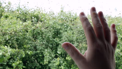 Ein-Mann-Mit-Seiner-Hand-Auf-Einem-Fenster-Mit-Regen-Draußen