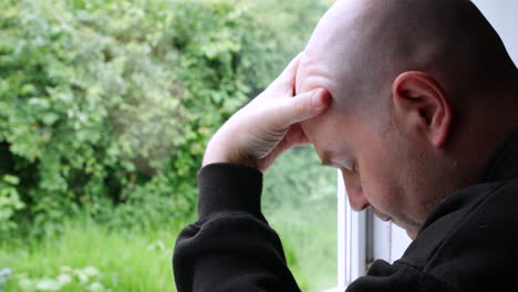 A-depressed-man-with-mental-health-problems-holding-his-head-in-his-hands-looking-out-of-a-window