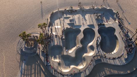 Aerial-view-of-people-at-the-Venice-beach-skate-park,-sunset-in-Los-Angeles,-USA---tilt-up,-drone-shot