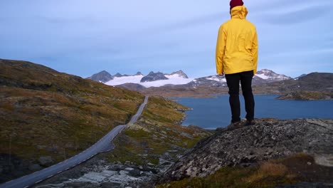 Man-in-yellow-raincoat-walking-on-a-rock-staring-into-the-distance