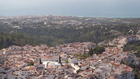 Slow-tilt-up-over-whitewashed-village-on-top-of-hill-with-ocean-in-distance