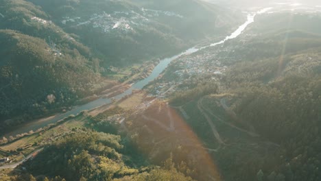 Aerial-view-of-river-next-to-mountains-and-villages,-during-the-sunset