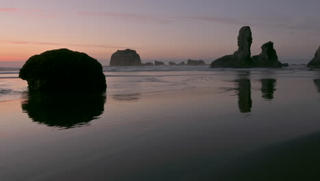 Silhouetted-rock-formations-in-Bandon-at-the-Oregon-Coast,-reflecting-in-wet-sand