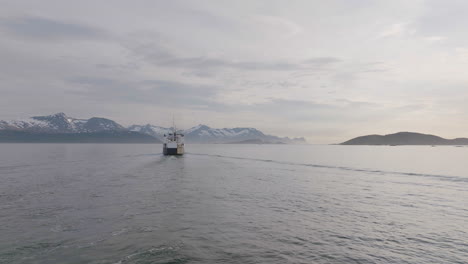 Amazing-scene-of-ferry-crusing-to-mountain-range-on-horizon,-Senja-Island,-Norway---aerial-birds-eye-view