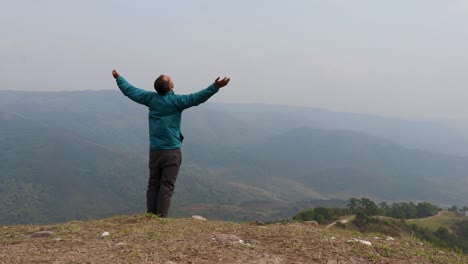 Mann,-Der-Die-Natur-Auf-Einem-Hügel-Mit-Nebligem-Bergwuthintergrund-Aus-Einem-Flachen-Winkelvideo-Genießt,-Wird-In-Nongjrong-Meghalaya,-Indien,-Aufgenommen