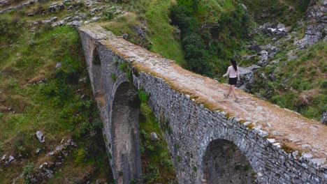 Aerial-of-young-girl-crossing-the-Ali-Pasha-aqueduct-bridge-during-trekking-in-the-mountains