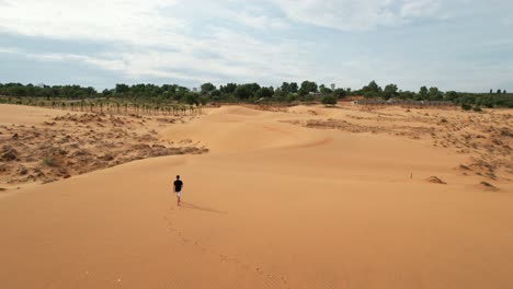 aerial-of-man-walking-on-top-of-desert-sand-dunes-toward-an-oasis-in-Mui-Ne-Vietnam