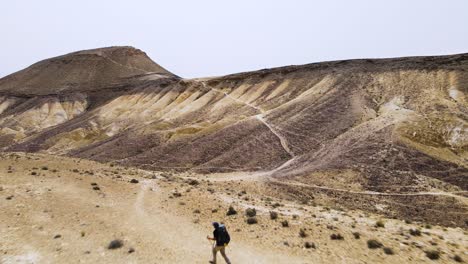 Dramatic-drone-shot-of-hiker-running-in-the-desert-walking-along-a-high-ridge-next-to-a-spectacular-Mountain-and-crater