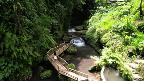 Frau-Im-Weißen-Kleid-Zu-Fuß-Auf-Einer-Bambusbrücke-Entlang-Eines-Flusses-Und-Wasserfalls-Im-Dschungel-Von-Bali-Indonesien