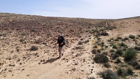 Fast-drone-fly-in-towards-hiker-walking-a-track-in-rocky-desert-wilderness-landscape