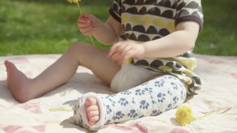 CLOSEUP,-PAN-UP-to-a-cute-toddler-playing-with-flowers-with-a-broken-leg