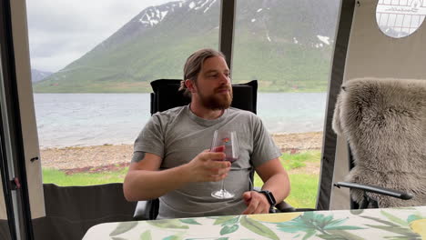 Static-shot-of-a-young-man-with-beard-drinking-wine-in-a-tent-during-a-heavy-storm-outside-in-summer-with-a-scenic-view