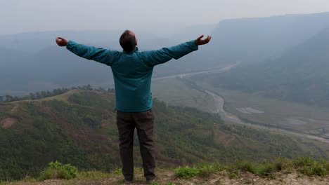 Hombre-Disfrutando-De-La-Naturaleza-En-La-Cima-De-La-Colina-Con-El-Fondo-De-La-Furia-De-La-Montaña-Brumosa-Desde-Un-Video-De-ángulo-Plano-Tomado-En-Nongjrong-Meghalaya-India