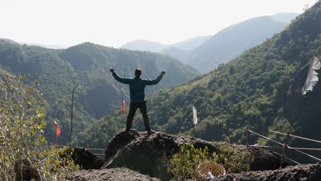 Isolierter-Junger-Mann-Auf-Bergspitze-Mit-Grünen-Wäldern-Und-Nebelblauem-Himmel-Am-Morgen-Aus-Einem-Flachen-Winkelvideo-Wird-Beim-Mawryngkhang-Trek-Meghalaya-Indien-Aufgenommen