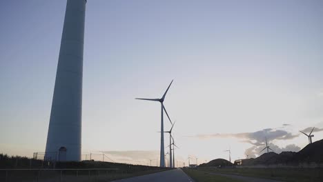 Driving-past-windmills-at-sunset,-giving-you-a-beautiful-image-of-renewable-energy