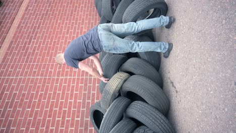 Caucasian-male-stacking-old-used-tires-in-front-of-a-brick-wall-to-be-recycled,-vertical
