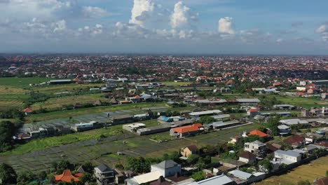 wide-aerial-of-rice-fields-after-a-harvest-in-bali-indonesia-and-dense-populated-neighborhoods-on-a-sunny-day
