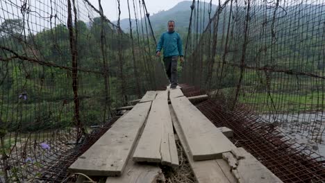 young-man-walking-at-vintage-iron-suspension-bridge-at-morning-from-flat-angle