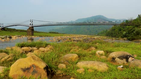 Puente-Colgante-De-Hierro-Aislado-Sobre-El-Río-Que-Fluye-Con-Fondo-De-Montaña-Y-Cielo-Azul-En-El-Video-De-La-Mañana-Se-Toma-En-Nongjrong-Meghalaya-India