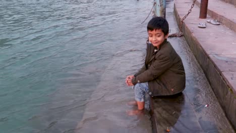 Niño-Aislado-Sentado-En-La-Orilla-De-La-Orilla-Del-Río-Santo-Ganges-Desde-Un-ángulo-Plano-Se-Toma-Un-Video-En-La-Orilla-Del-Río-Ganga-Rishikesh-Uttrakhand-India