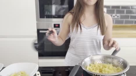 Young-female-making-pasta-and-sauce-in-a-large-kitchen-late-at-night,-smiling-at-the-camera-and-getting-embarrassed-and-camera-shy