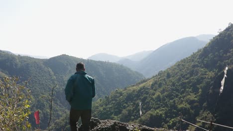 Isolierter-Junger-Mann-Auf-Bergspitze-Mit-Grünen-Wäldern-Und-Nebelblauem-Himmel-Am-Morgen-Aus-Einem-Flachen-Winkelvideo-Wird-Beim-Mawryngkhang-Trek-Meghalaya-Indien-Aufgenommen