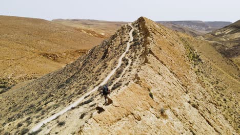 Dramatic-drone-shot-of-hiker-in-the-desert-walking-along-a-high-ridge-with-view-to-a-spectacular-Mountain-and-crater