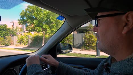 A-mature-man-in-glasses,-casual-clothes,-and-a-cap,-driving-a-car-and-talking