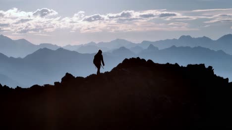 Female-mountaineer-walking-on-a-ridge-backlit-by-the-sun-and-other-mountains-in-the-background