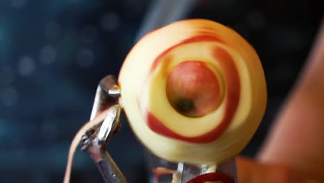 An-out-of-focus-person-using-a-hand-crank-peeler-to-peel,-core,-and-slice-an-organic,-homegrown-apple