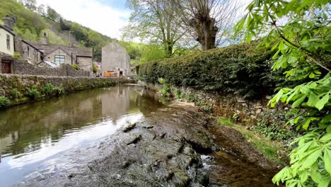 Stream-running-slowly-over-rocks-with-Castleton-village-in-the-background