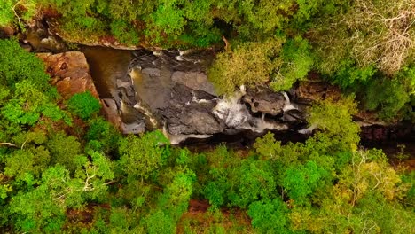 Birds-eye-aerial-view-over-a-rocky-water-fall-in-a-river-in-the-middle-of-a-forest