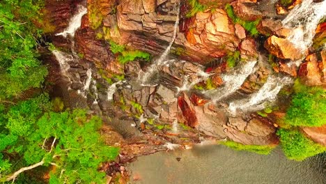 Birds-eye-aerial-shot-flying-up-over-a-cliff-with-water-streaming-down