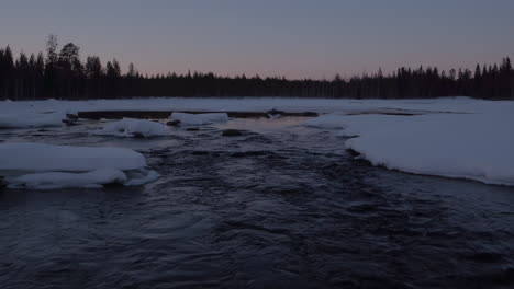 Cinematic-low-level-aerial-shot-of-a-snowy-stream-at-dusk