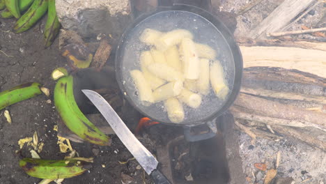 Overhead-view-of-plantains-boiling-in-a-pot-over-an-open-fire,-with-a-large-knife-sitting-beside-the-pot