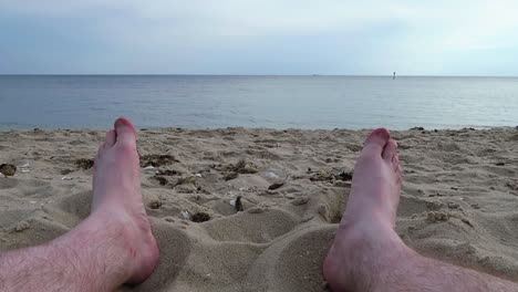 Mans-feet-wiggling-on-Hampton-beach,-day-time