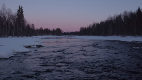 Dynamic,-cinematic-low-level-aerial-shot-up-an-icy-river-at-dusk