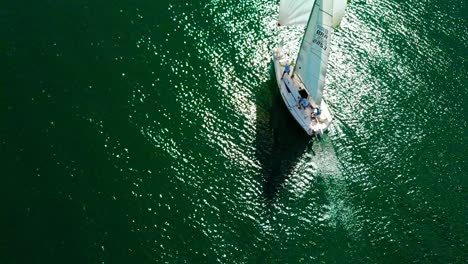 Birds-eye-view-of-a-small-sail-boat-on-open-water-with-the-sun-reflecting-on-the-waves
