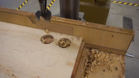 Close-up-clip-of-a-hand-sweeping-away-wood-shavings-after-drilling-a-hole-in-plywood-with-a-drill-press