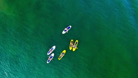 A-group-of-young-friends-hang-out-on-paddle-boards-on-the-water,-drone-shot