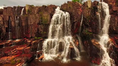 Drone-shot-flying-towards-and-over-a-small-waterfall-along-a-rocky-cliff-face