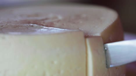 Knife-cutting-round-cheese-wheel,-closeup-shot