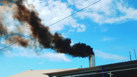 Black-smoke-billowing-out-of-steel-chimney,-blue-sky-background
