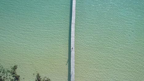 Aerial,-top-down,-birdseye,-drone-shot-of-people-walking-on-a-wooden-pier,-at-a-paradise-beach,-on-a-sunny-day,-in-Koh-Kood,-Thailand,-Asia