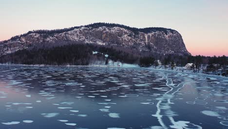 Aerial-view-of-a-frozen-lake-at-sunrise-with-long-cracks-and-circular-patterns-flying-towards-an-isolated-mountain