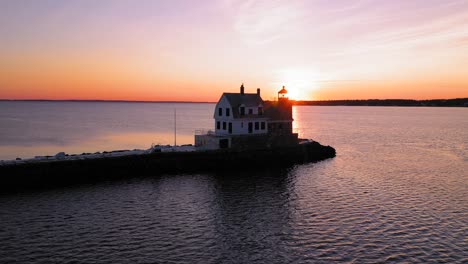 Low-and-slow-aerial-SLIDE-past-a-backlit-lighthouse-at-the-end-of-a-breakwater-revealing-the-bright-sunrise-behind-it