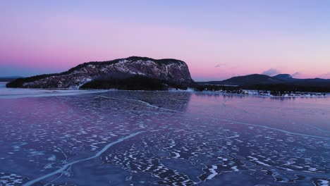 Aerial-view-of-a-frozen-lake-at-sunrise-flying-towards-an-isolated-mountain
