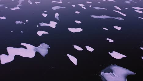 Close-up-Aerial-TOP-DOWN-view-of-the-dark-ice-of-a-frozen-lake-with-small-islands-of-snow-at-dawn