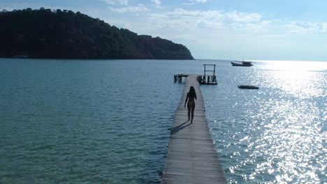 Female-walking-alone-on-a-pier-in-the-ocean-on-a-tropical-island,-koh-kood,-Thailand