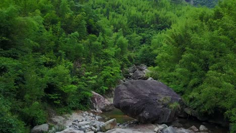Somber-drone-shot-over-eroded-rocks-between-beautiful-green-trees-in-a-forest-area